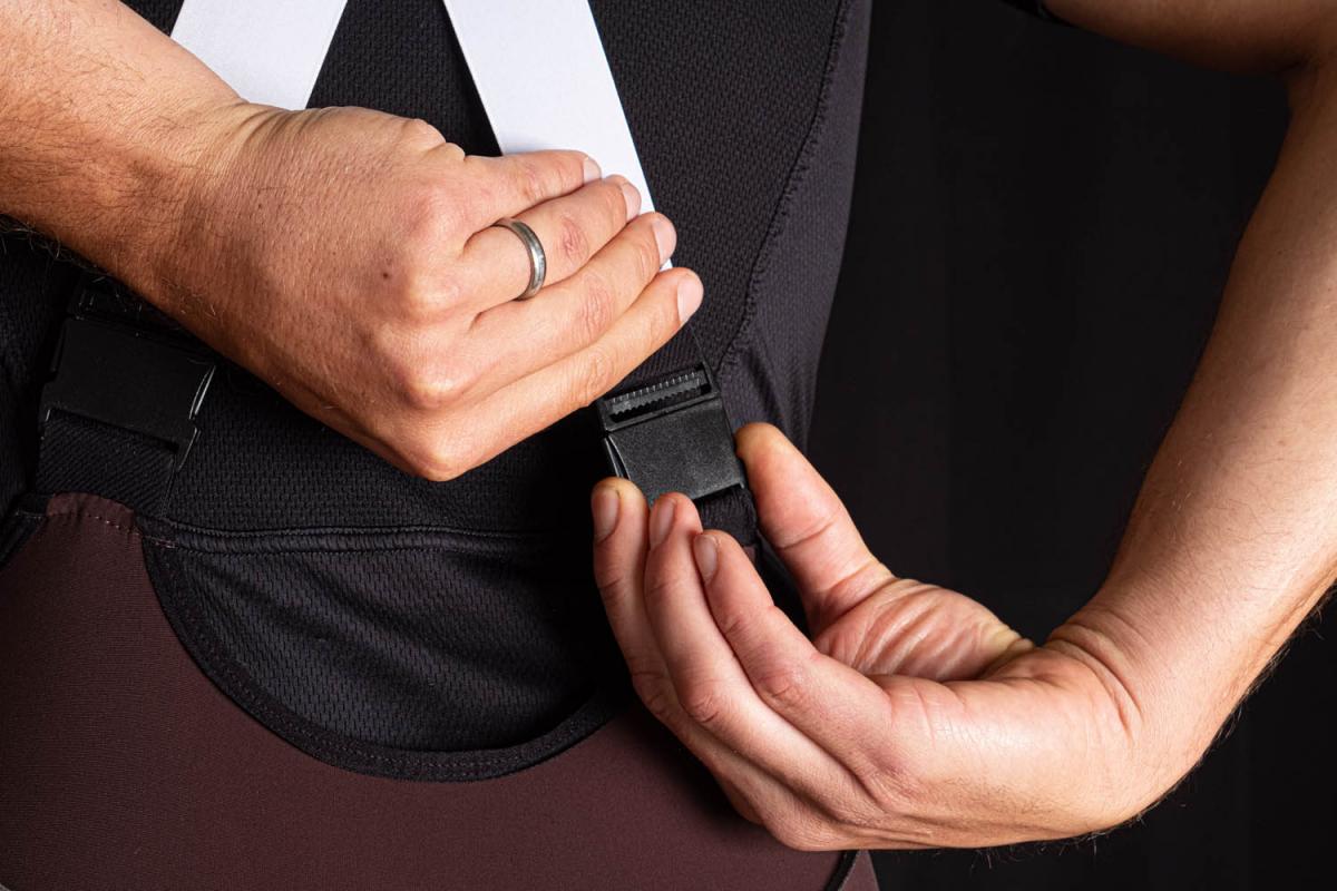 Close-up of hands adjusting a black buckle on a cycling bib with white straps.