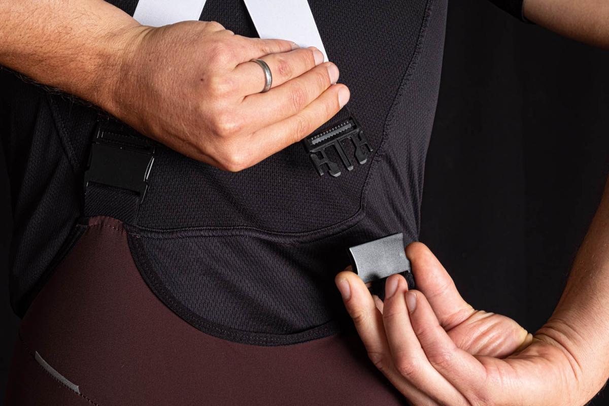 A close-up view of a person fastening a strap on a cycling jersey, showcasing black and white fabric with a prominent buckle.