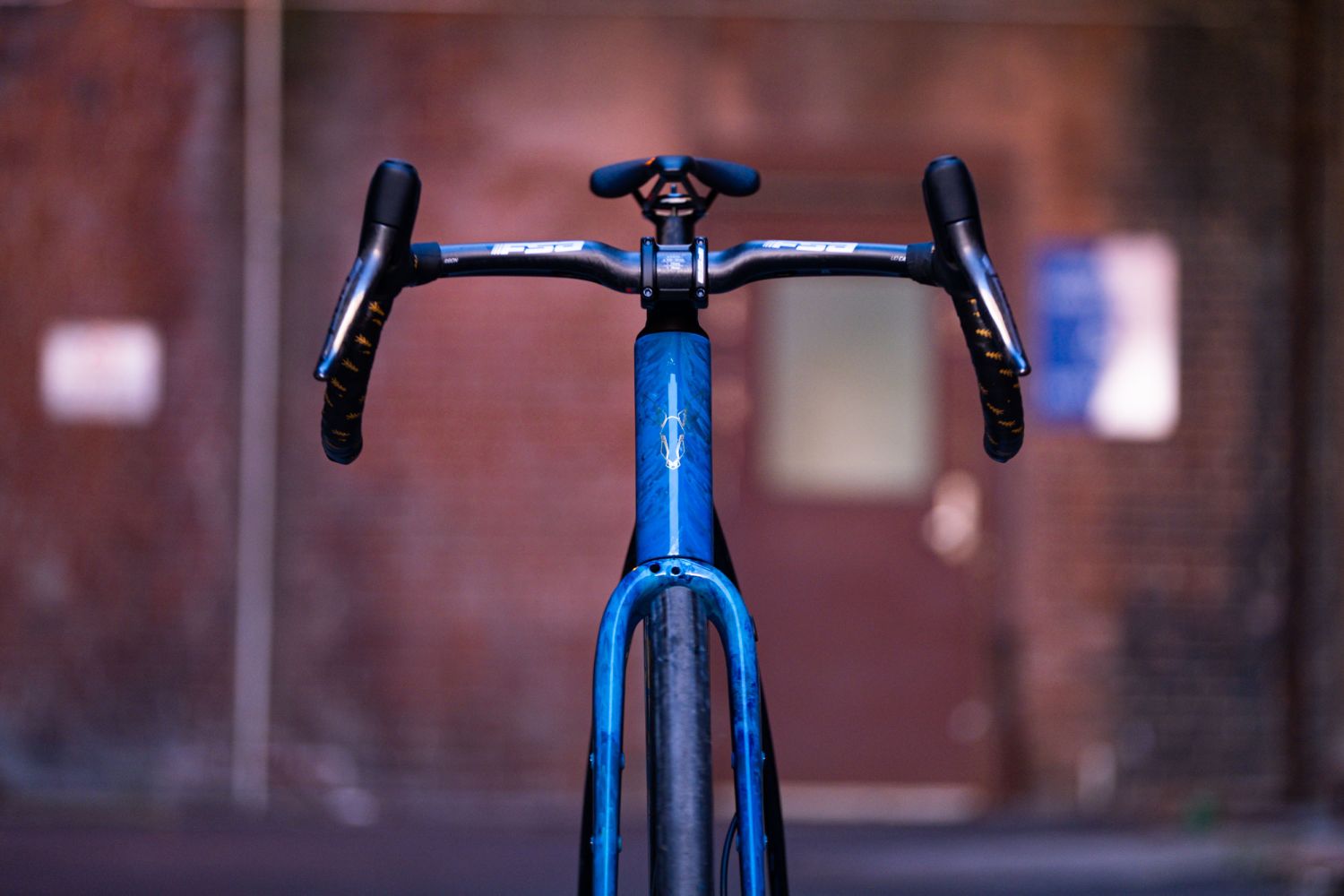 Close-up view of the handlebars and front frame of a blue bicycle against a rustic brick background.