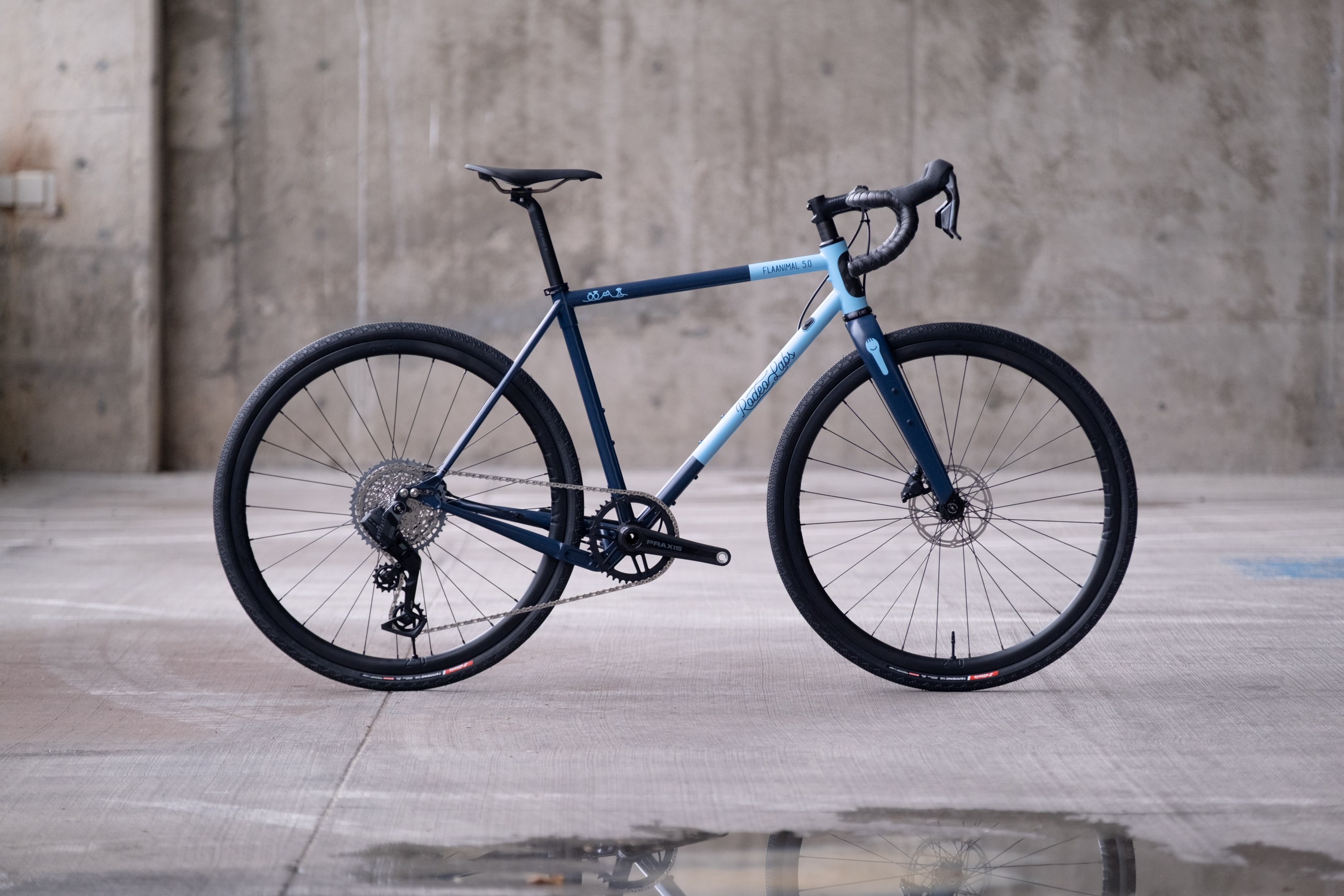 A blue and black gravel bike positioned on a concrete surface.