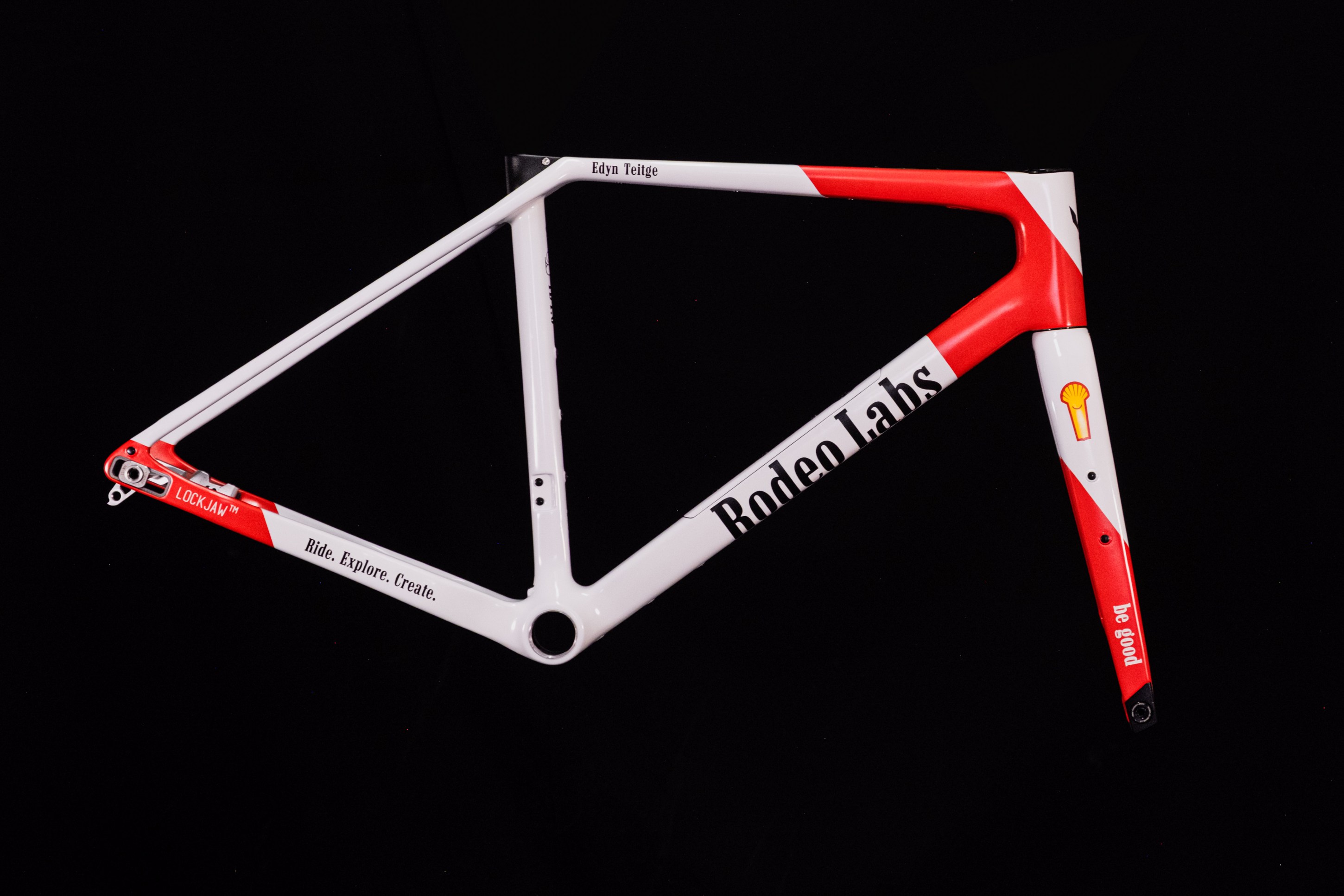 A bicycle frame designed by Rodeo Labs, featuring a red and white color scheme with the text 'Ride. Explore. Create.' and 'be good.' on it.