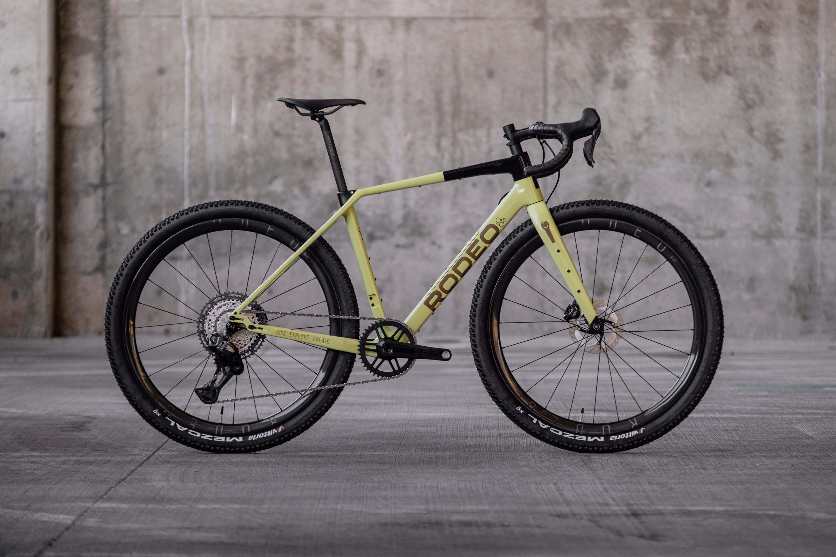Side view of a yellow and black gravel bike with thick tires and modern design, set against a concrete background.