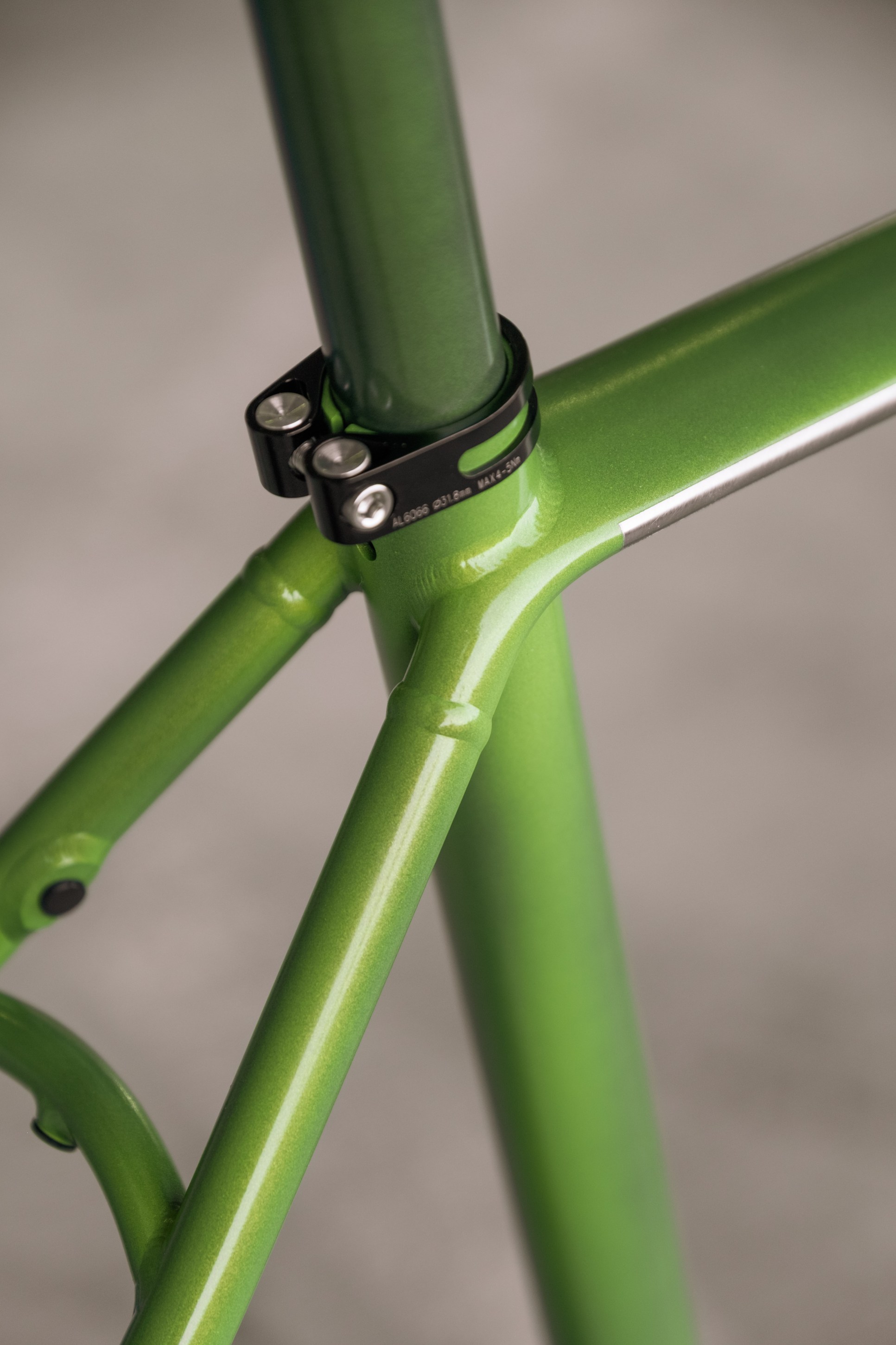 Close-up of a green bicycle frame featuring a polished finish, highlighting the seat post clamp and joinery details.