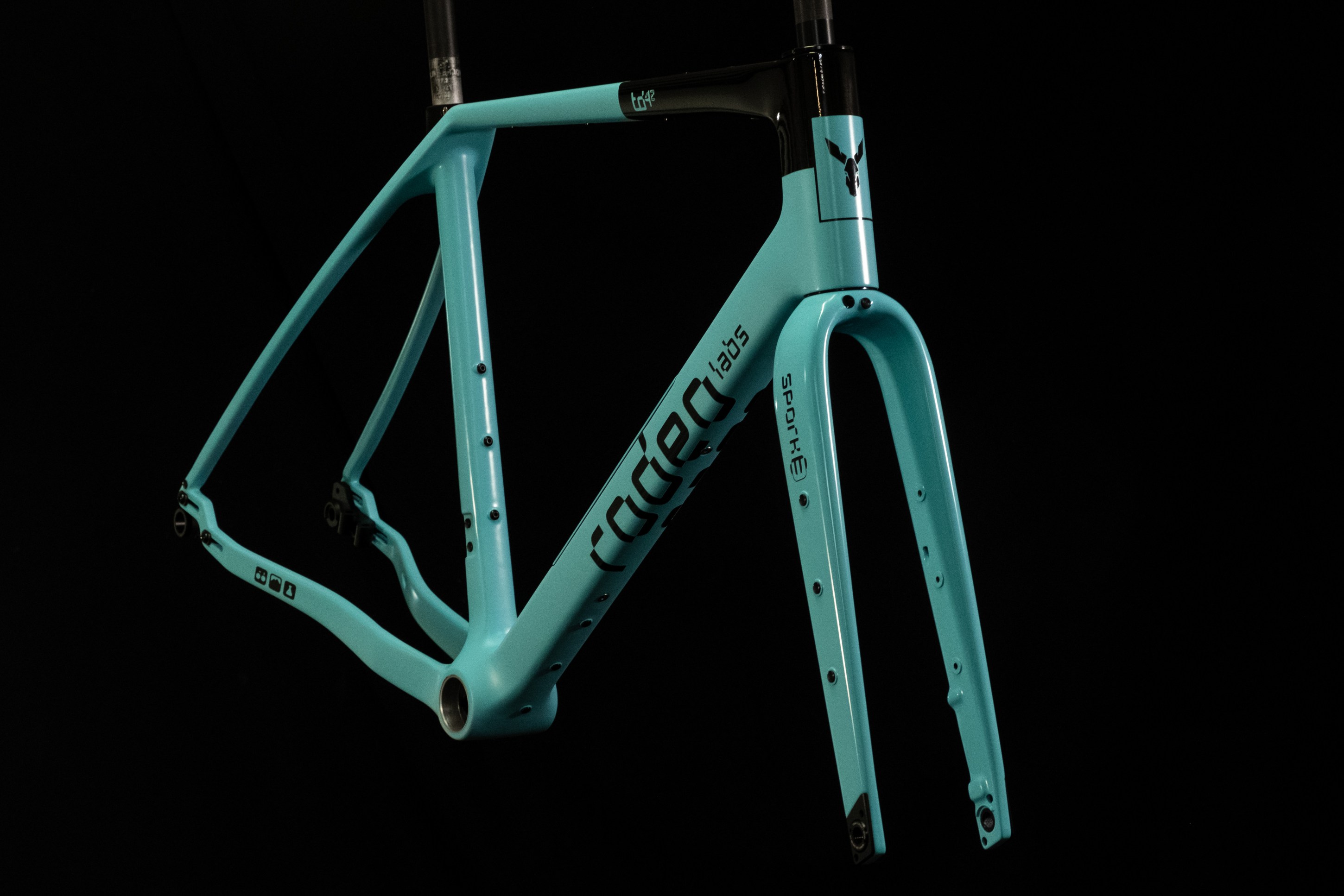 A teal bicycle frame with black accents, displaying various mounting points, photographed against a black background.