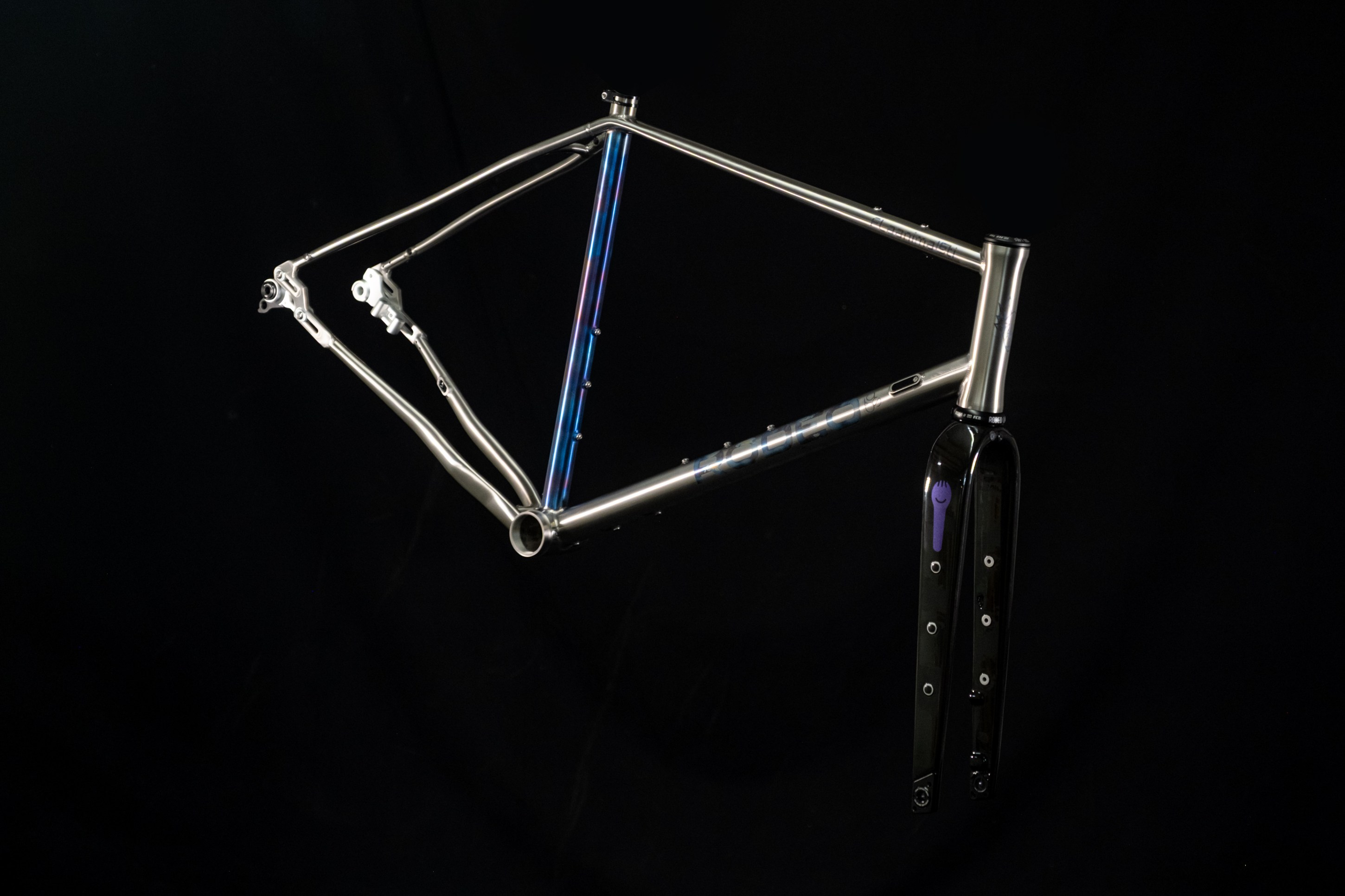 A metallic bicycle frame showcased against a black background, featuring a sleek design and a black fork with a purple accent.
