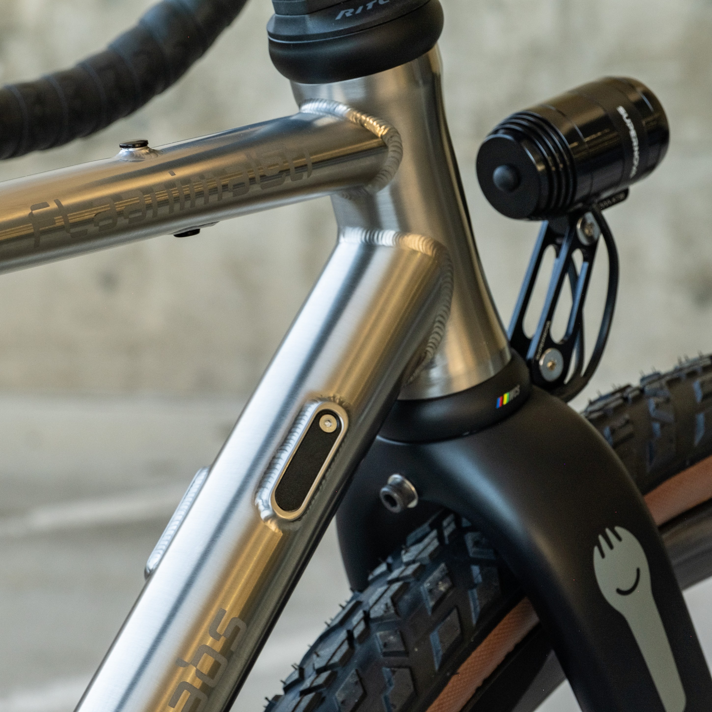 Close-up of a bicycle frame showcasing a metallic finish, with a mounted black bike light and textured tires.