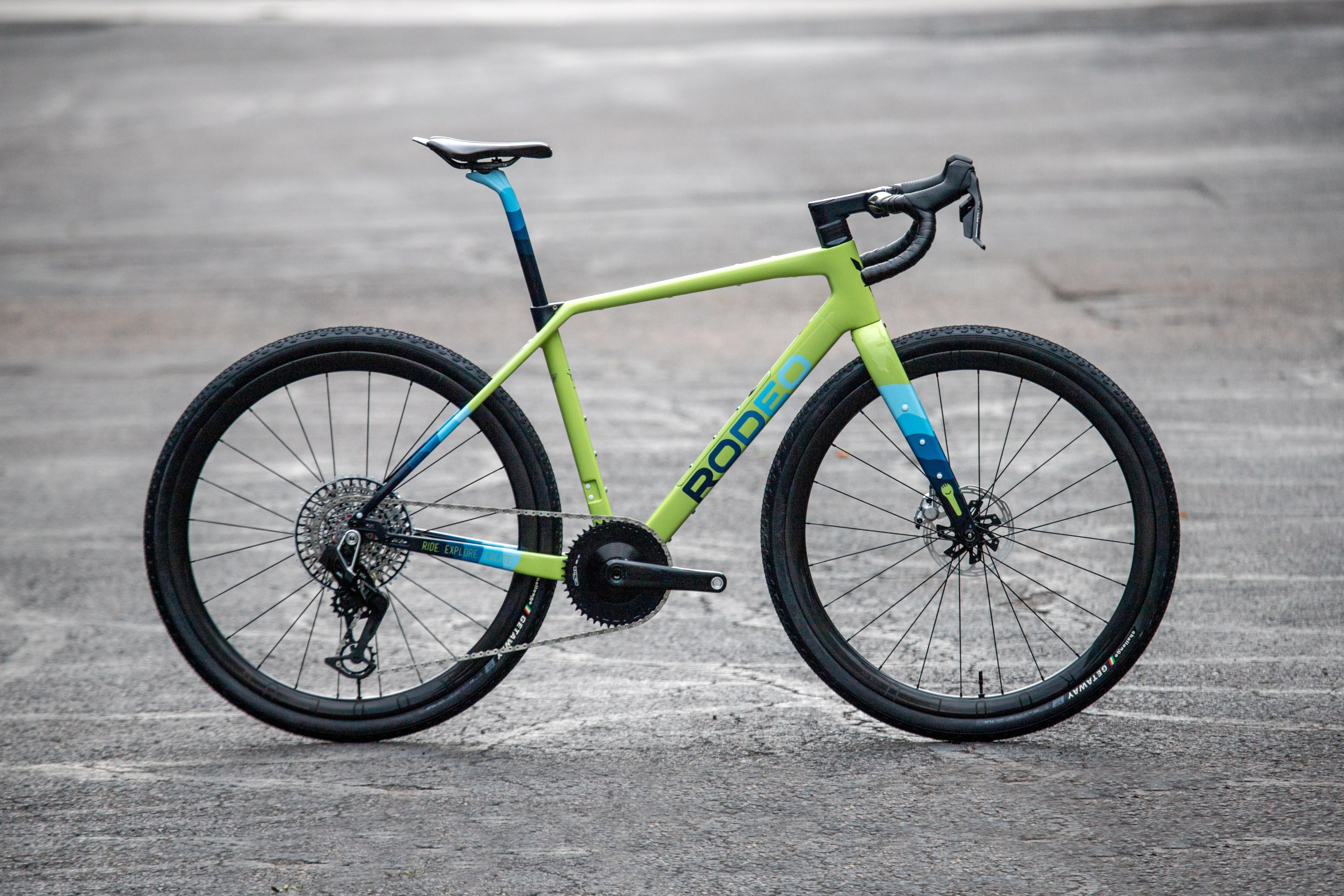 A vibrant green and blue gravel bike with a modern design, featuring disc brakes and wide tires, positioned on a concrete surface.