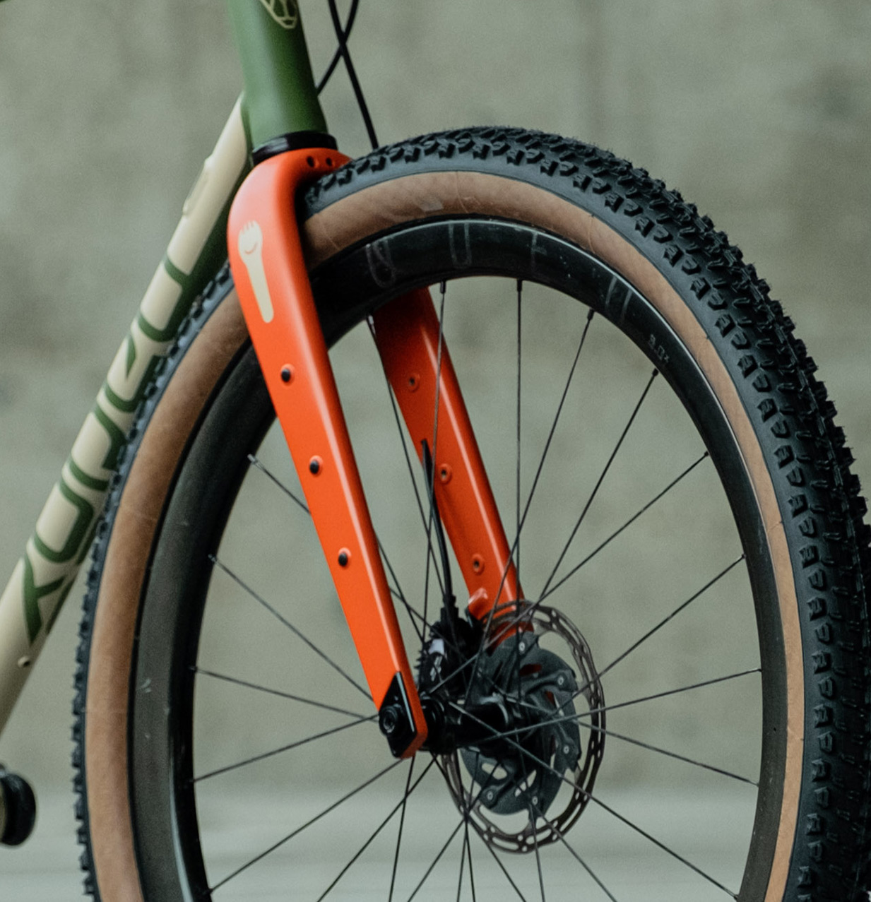 Close-up of a bicycle front fork with an orange finish, featuring disc brakes and a textured tire.