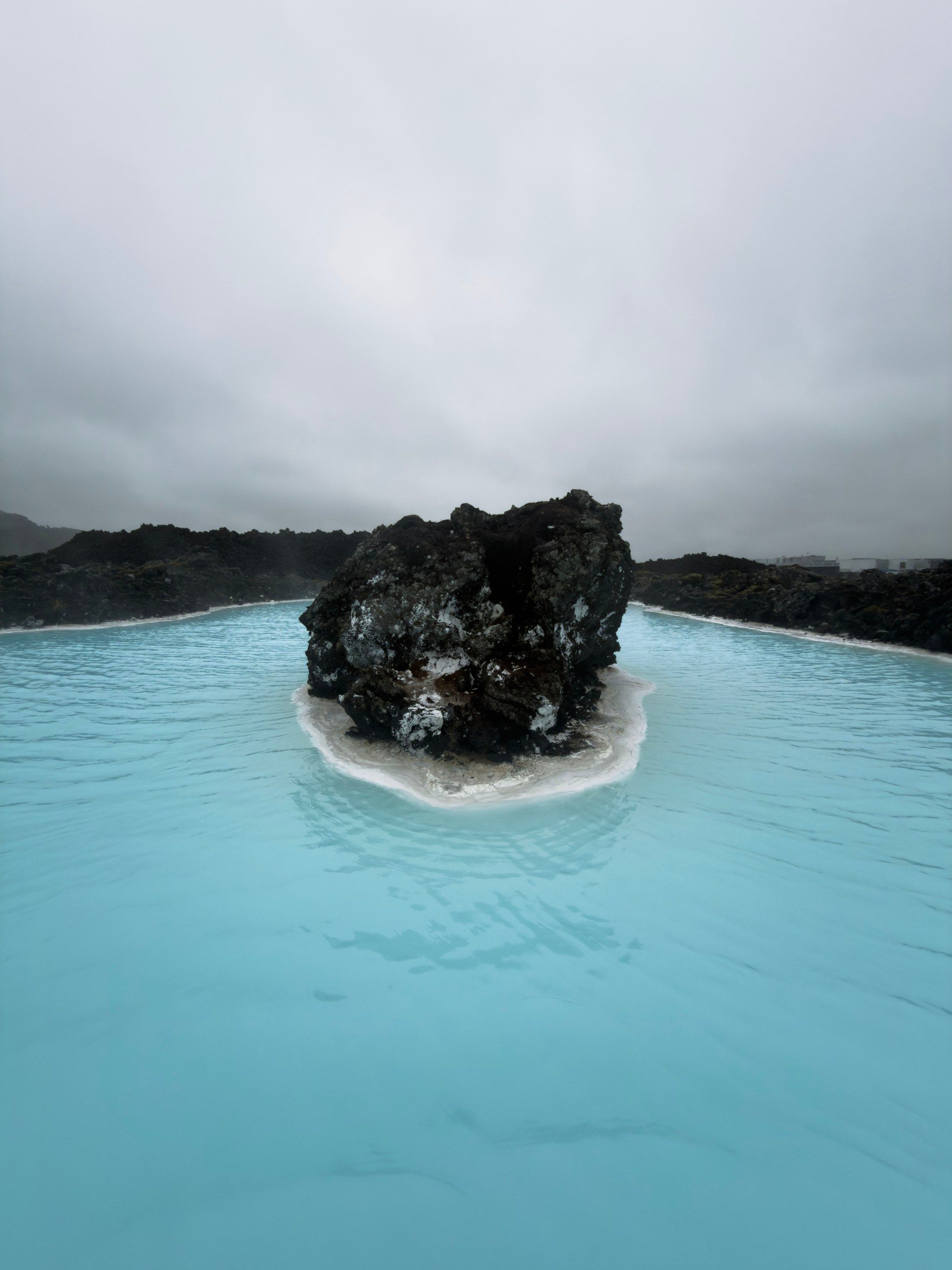 A rocky outcrop surrounded by light blue water under a cloudy sky.