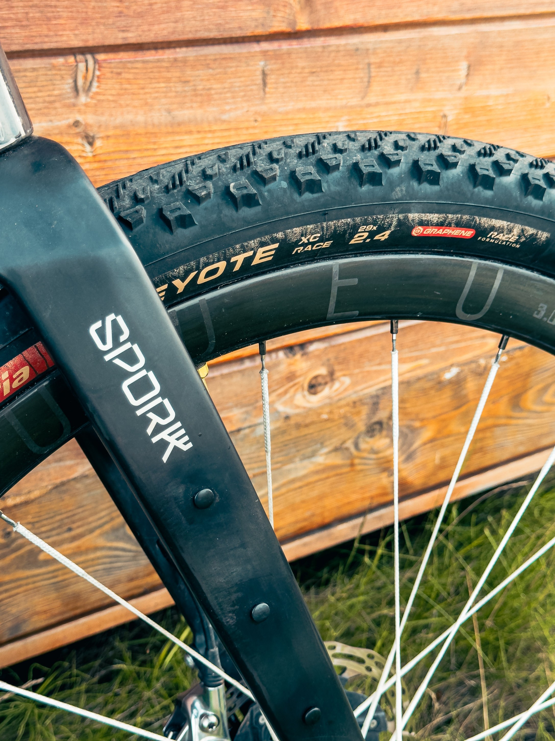 Close-up of a mountain bike wheel featuring a Spork fork and a Coyote XC Race tire, set against a wooden background.