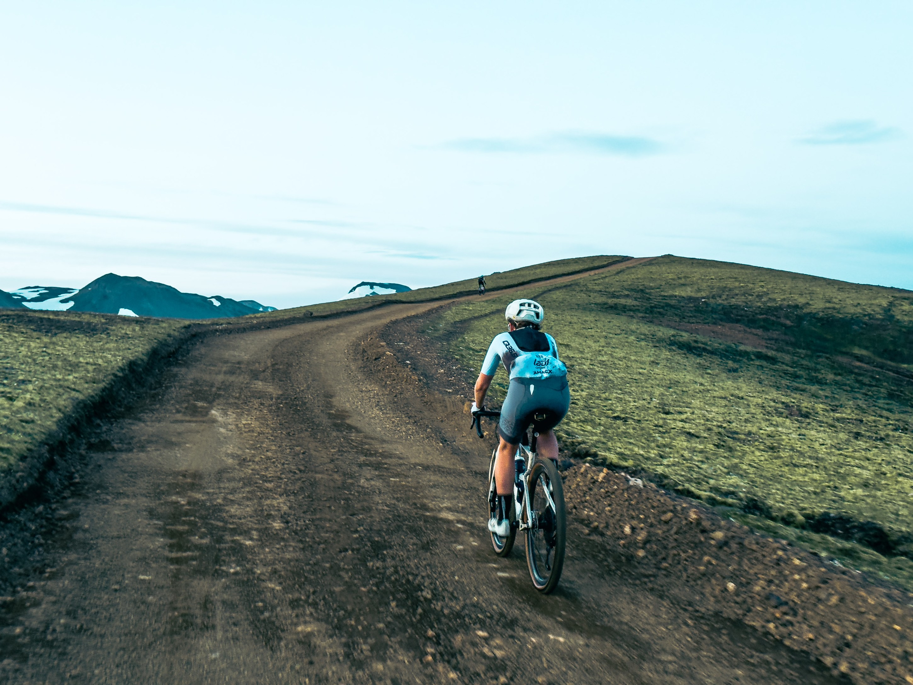 A cyclist riding along a dirt road in a rugged mountainous landscape under a clear sky.