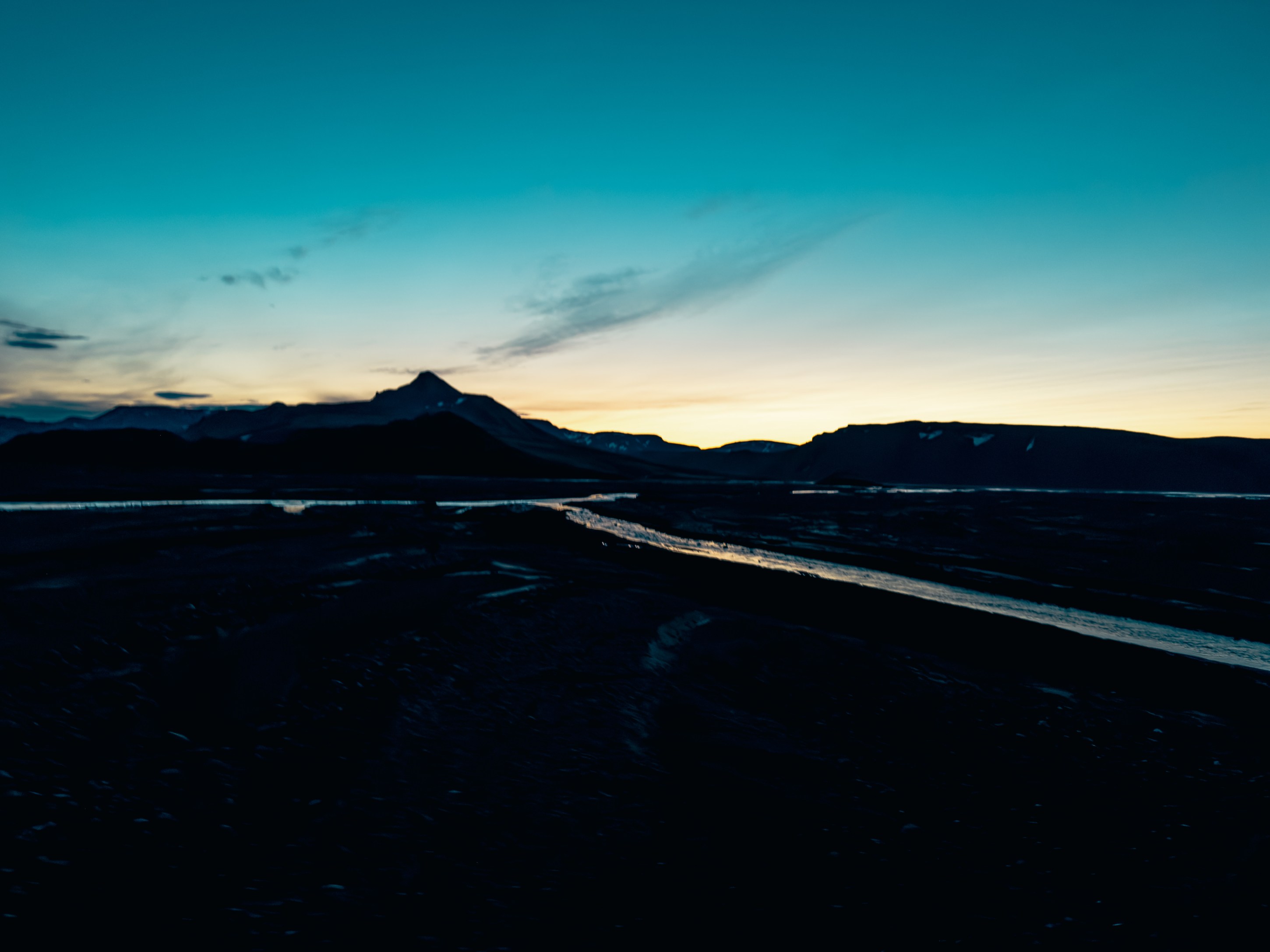 A dramatic sunset over a mountain silhouette with a flowing river in the foreground, set against a gradient sky transitioning from blue to orange.