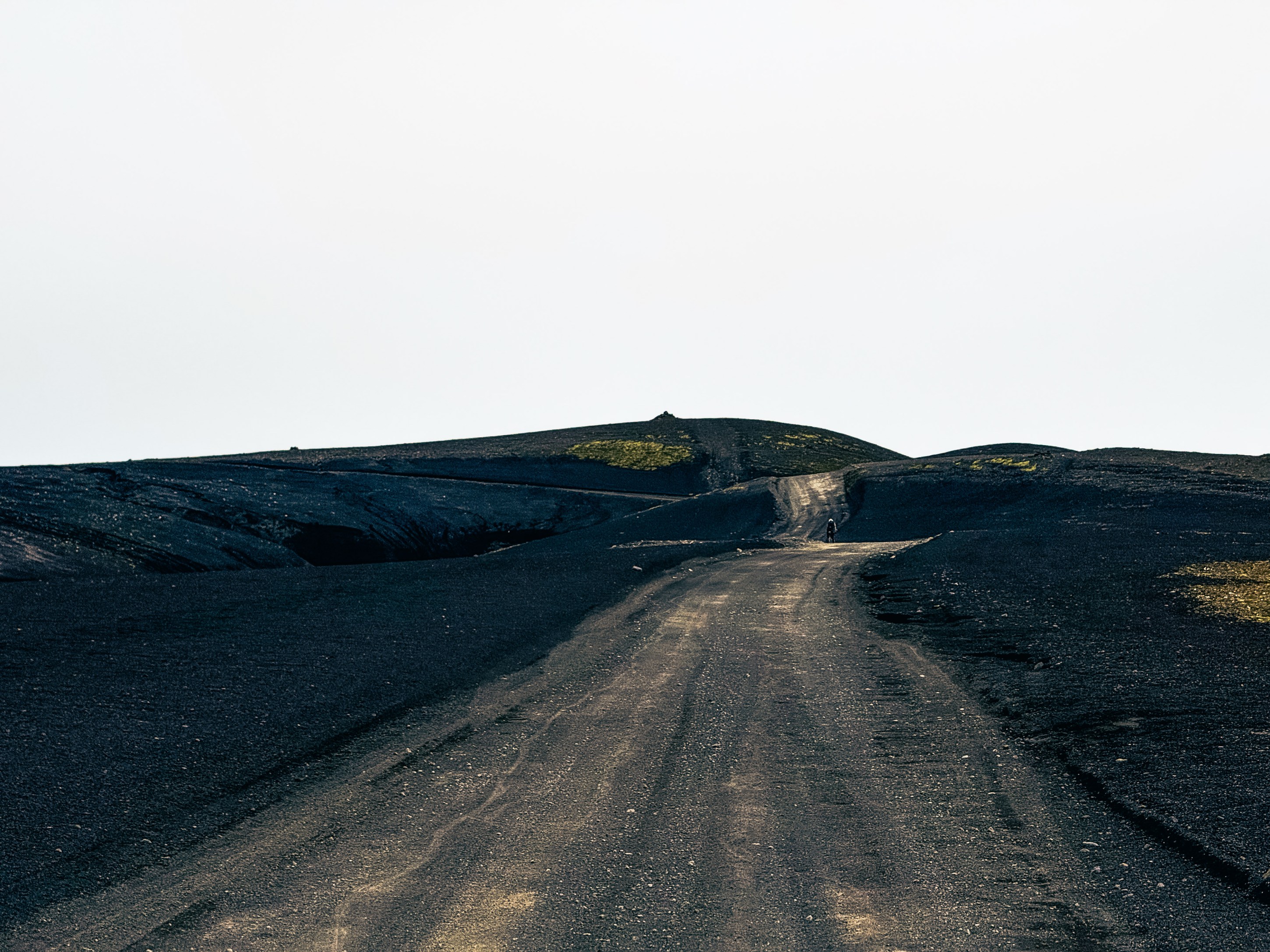 A winding dirt road on a volcanic landscape with dark black soil and a hint of green vegetation in the background.