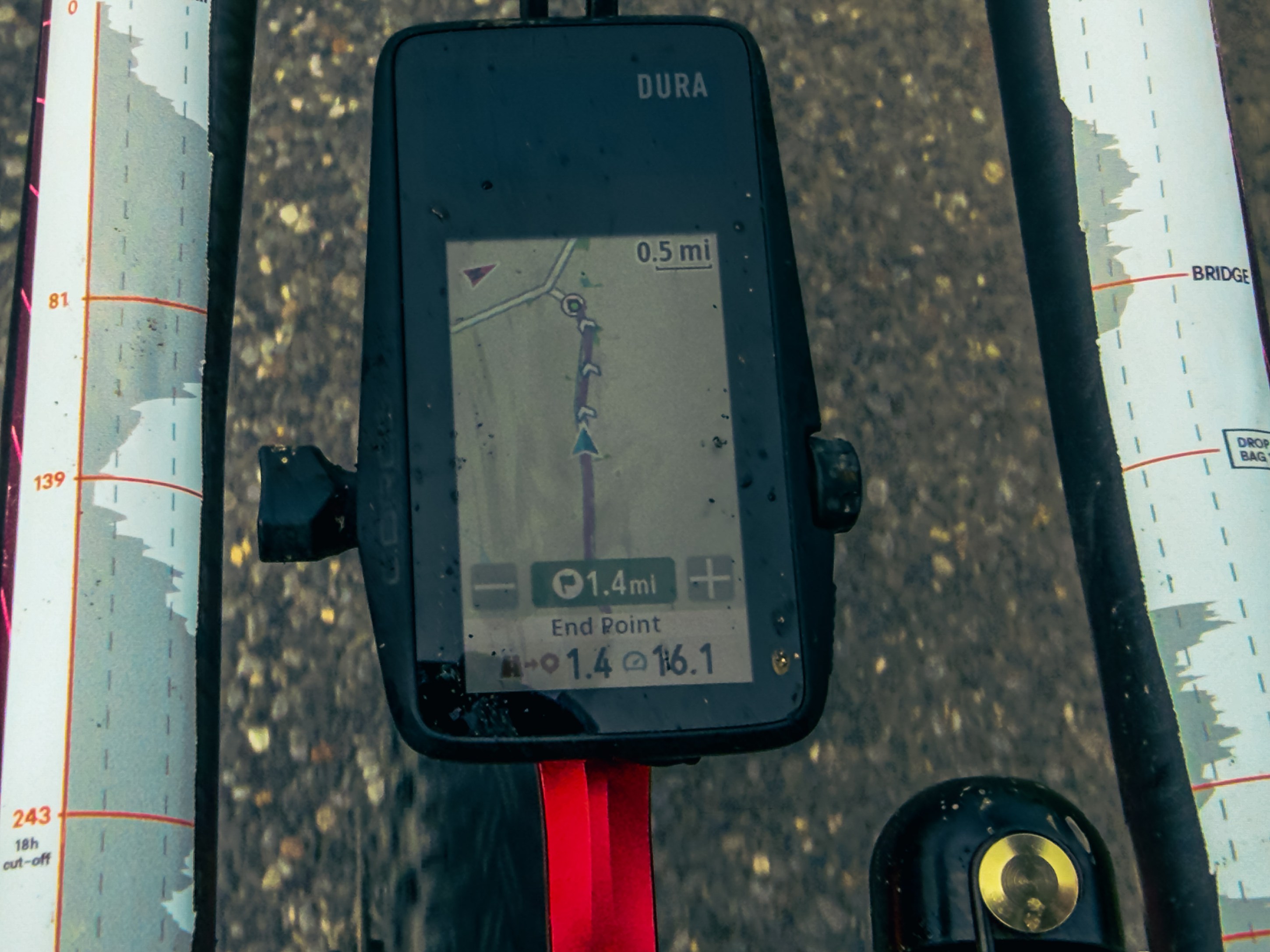 A close-up view of a cycling GPS device displaying navigation information, showing a distance of 0.5 miles to the next turn and 1.4 miles to the end point, mounted on a bicycle handlebars.