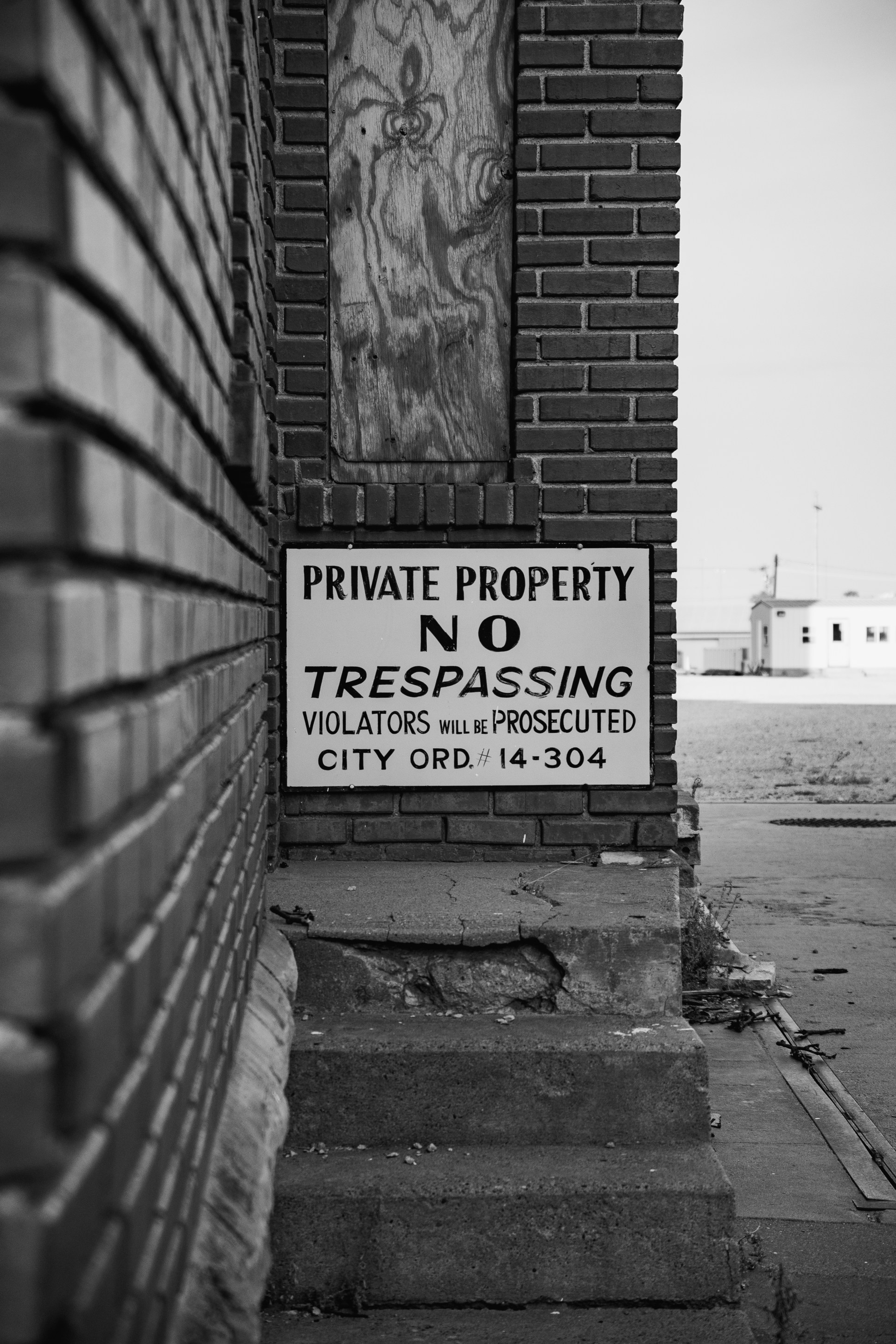 Close-up view of a 'No Trespassing' sign on a brick wall, indicating private property. The sign details that violators will be prosecuted.