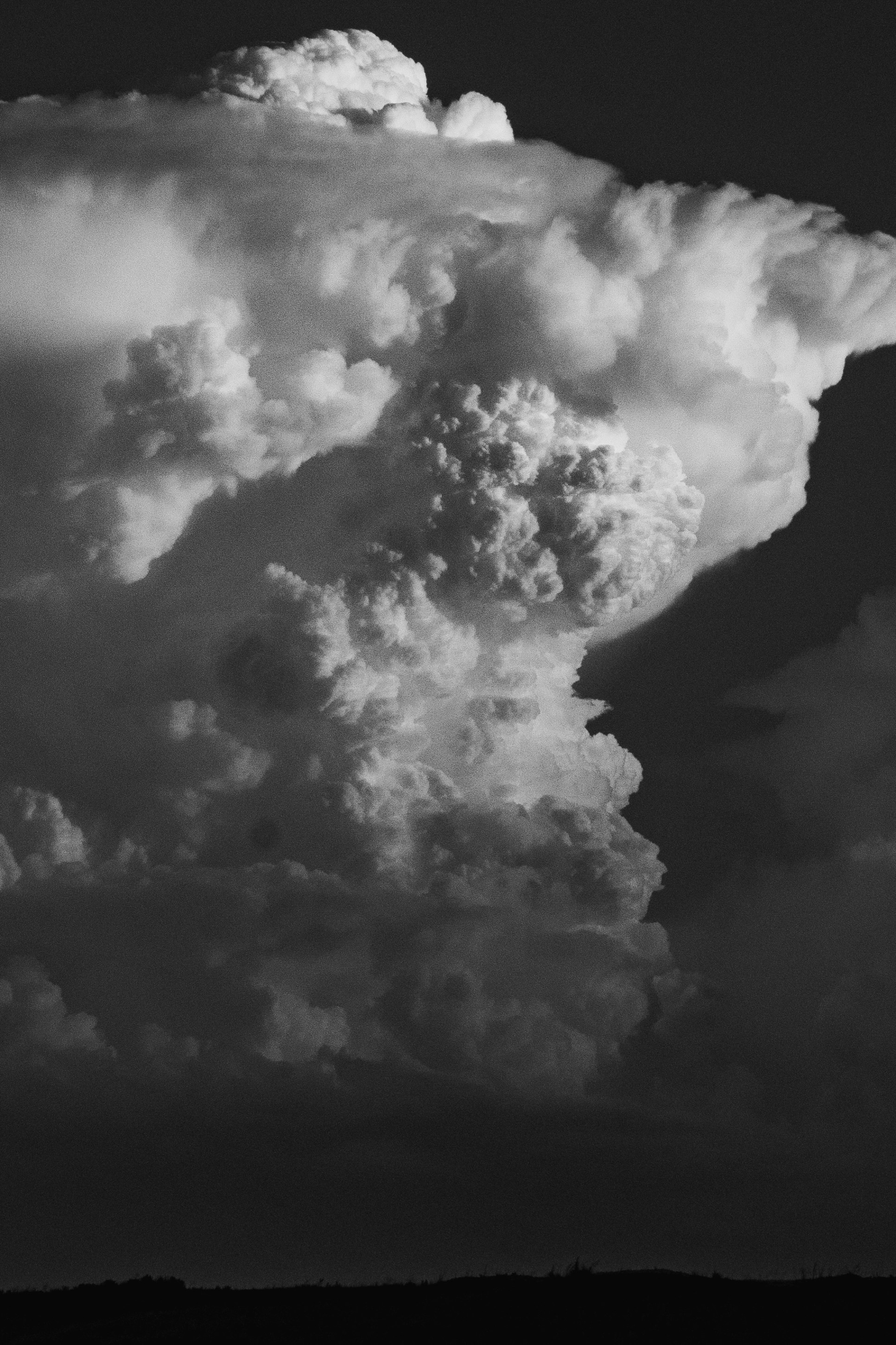 Dramatic black and white image of billowy, swirling clouds against a dark background, resembling a towering storm cloud.