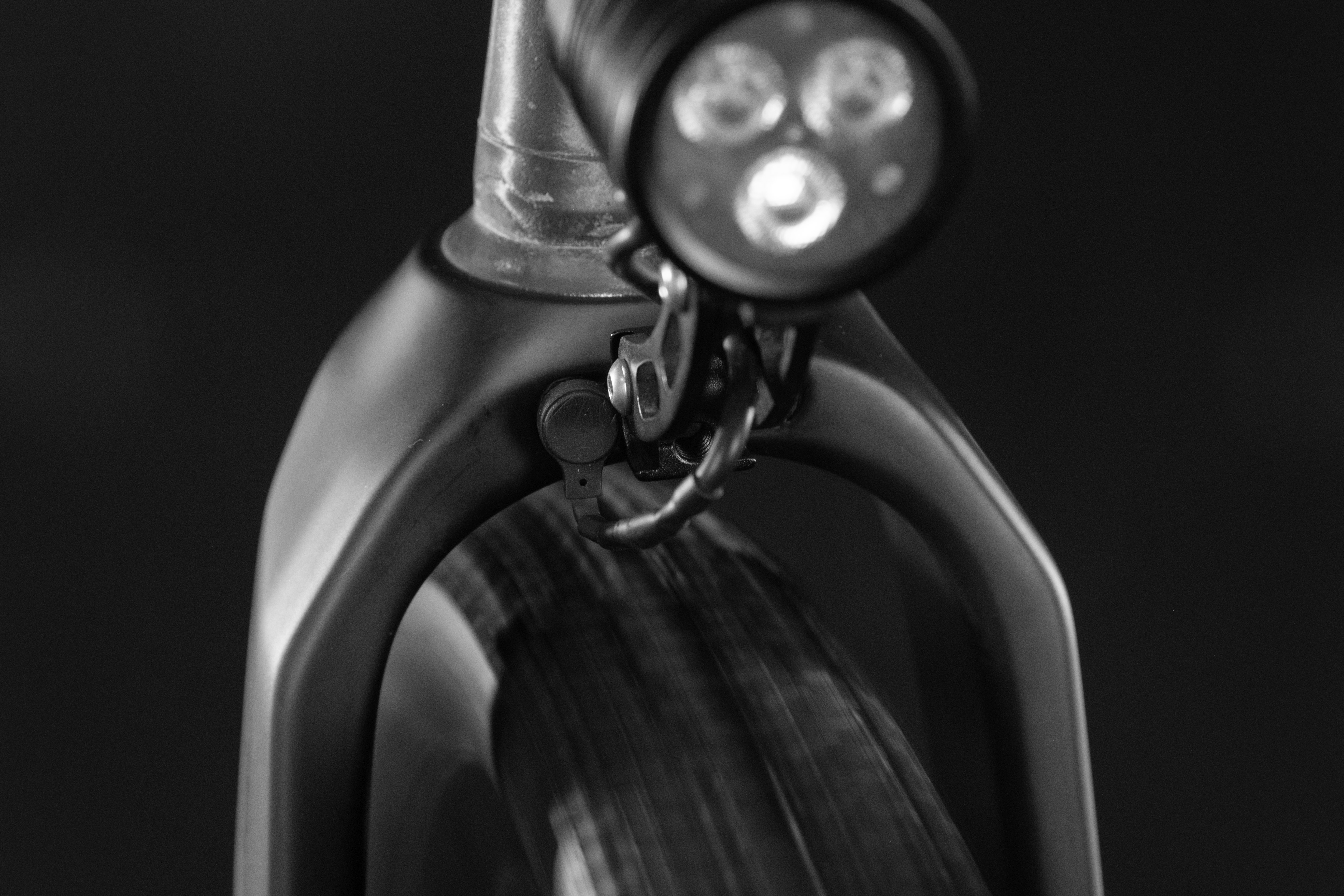 Close-up view of a bicycle front fork and light, with a blurred tire in the background.