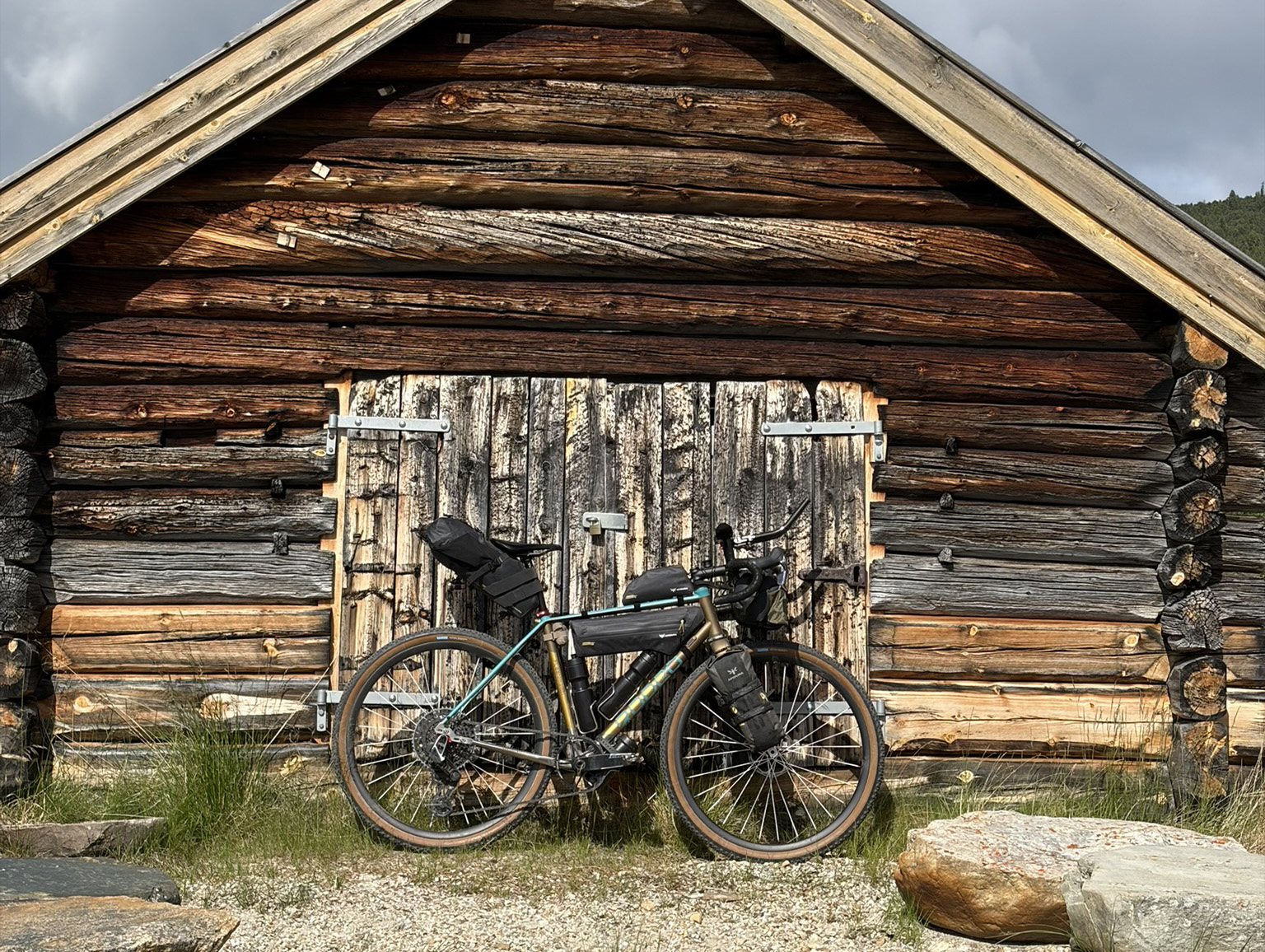 A bicycle parked in front of a rustic wooden cabin with a textured log exterior and a closed wooden door.