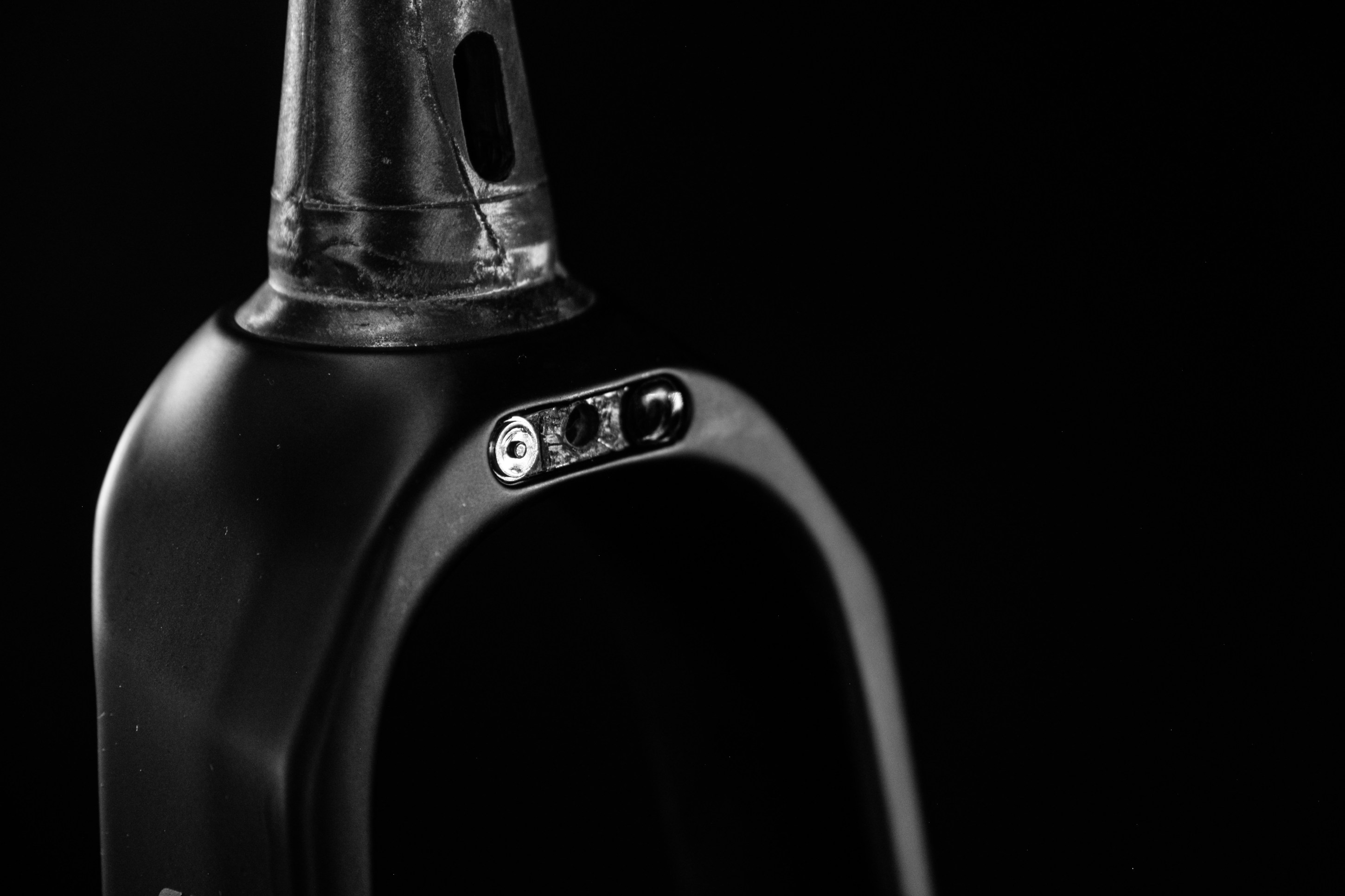 Close-up of a black object with a curved shape, featuring a prominent attachment point and details like screws, against a dark background.